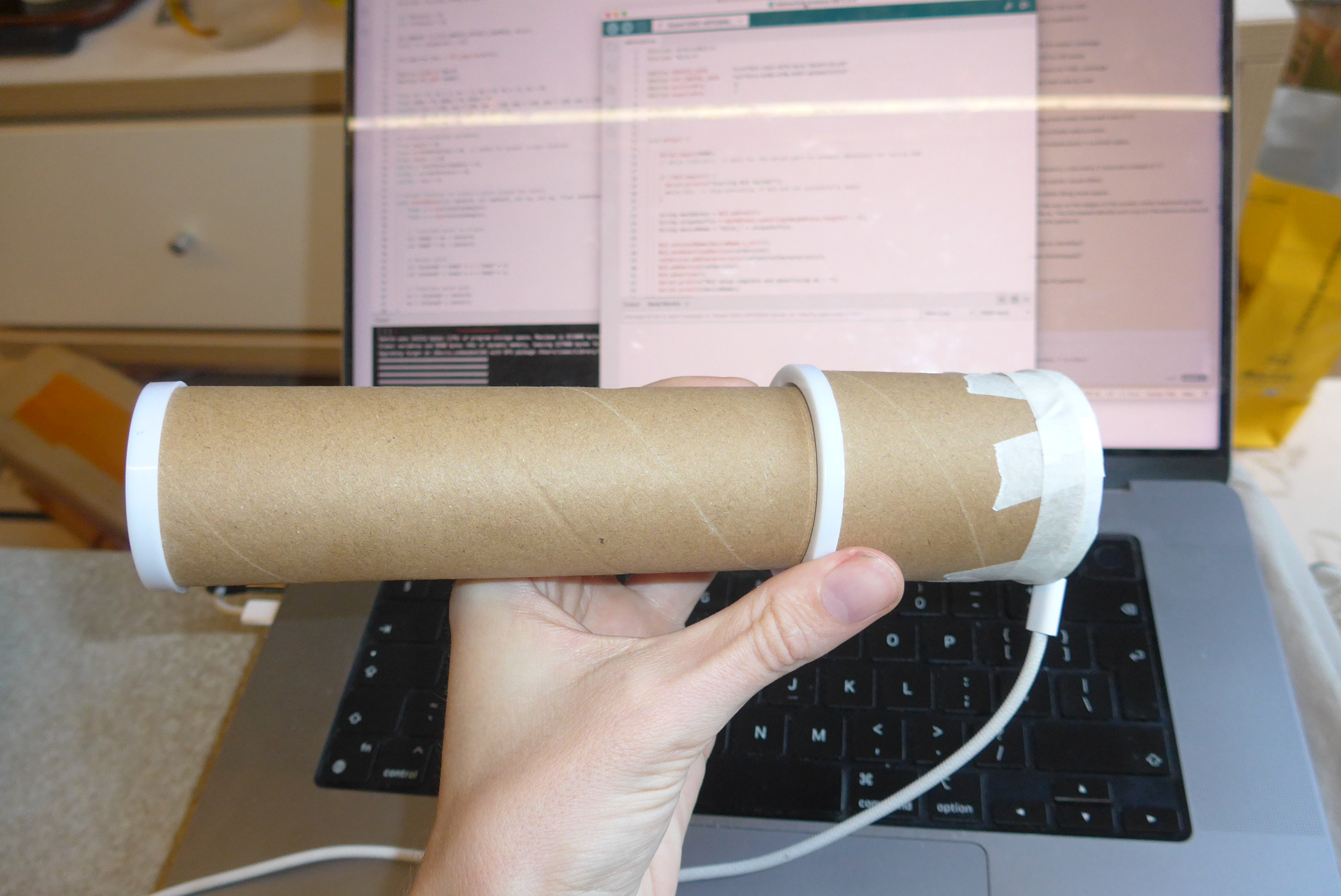 Cardboard tube prototype held in front of a laptop running code