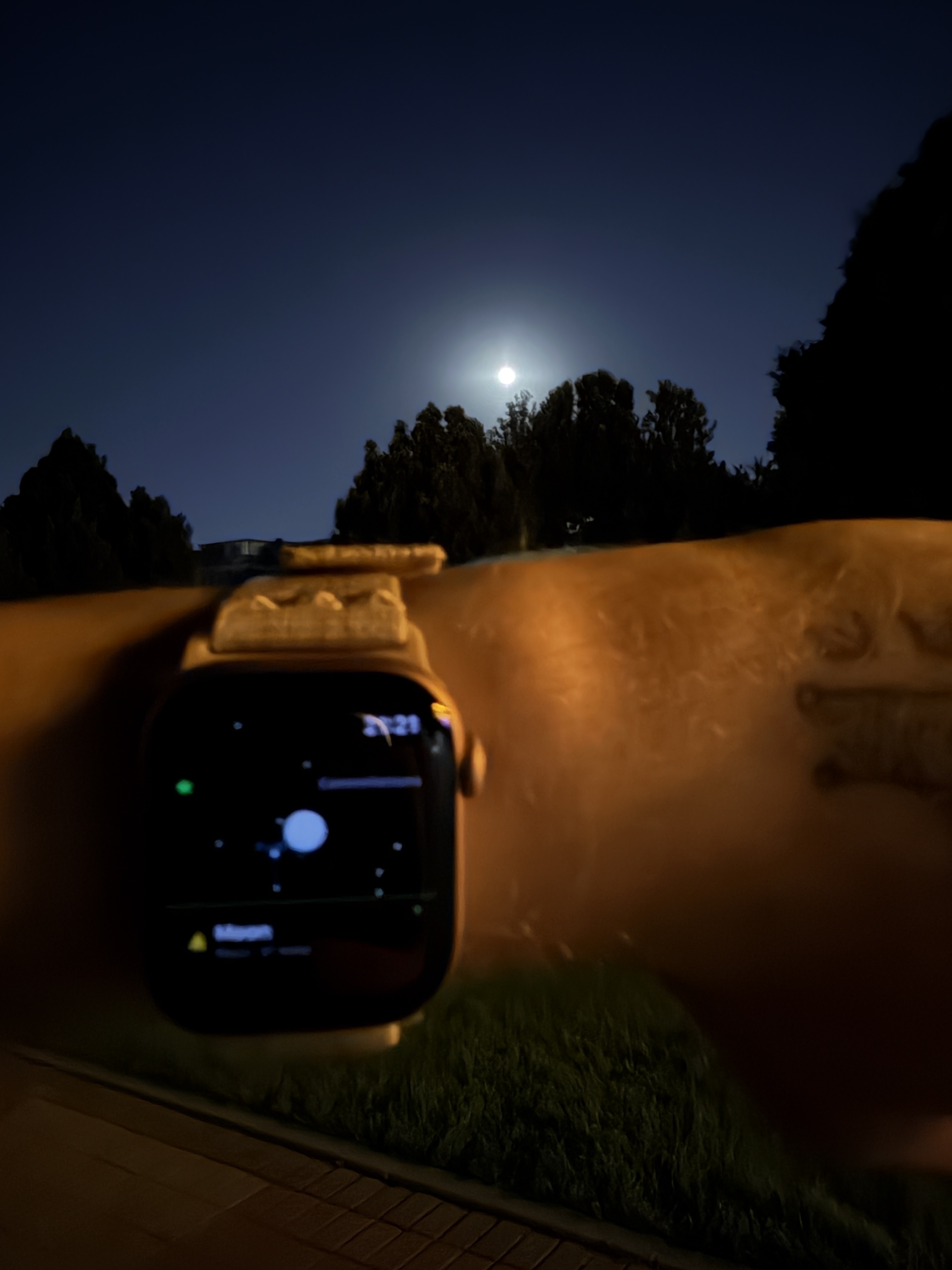 An Apple Watch held up to a night sky with the Moon visible, the screen showing a star map